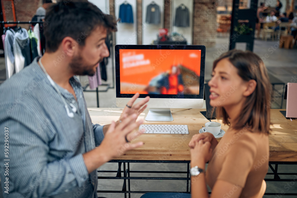 Young man and woman talking in front of desktop computer in a clothing shop. Business meeting. Young man and woman talking in front of desktop computer in a clothing shop. Business meeting.