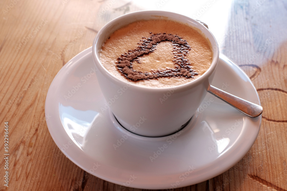 Cappuccino coffee in white cup with beautiful heart shape latte art on wooden table.