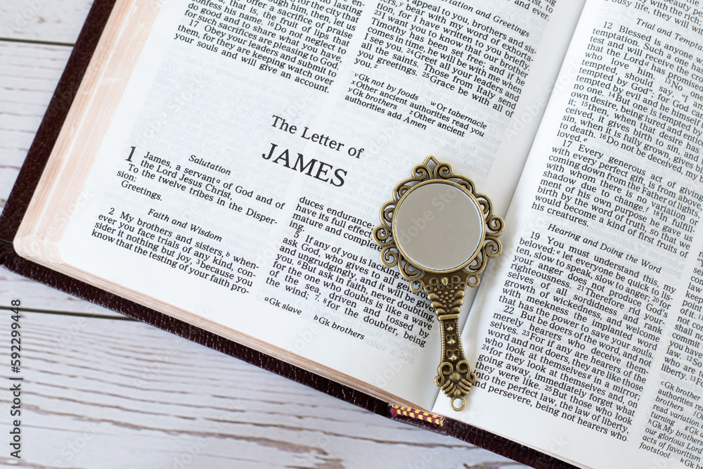 Open holy bible book of James with ancient golden mirror on wooden