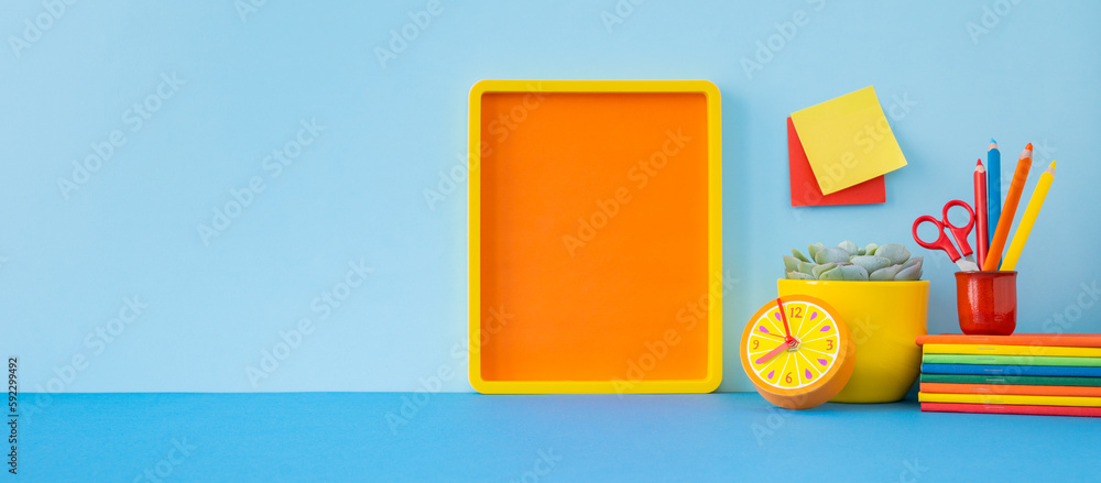 Creative desk with a blank picture frame, desk objects, school supplies, books, and plant on a pastel blue background.
Creative desk with a blank picture frame, desk objects, school supplies, books, and plant on a pastel blue background.