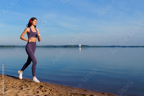 A woman runs along the sea and listens to music. Cardio training outside