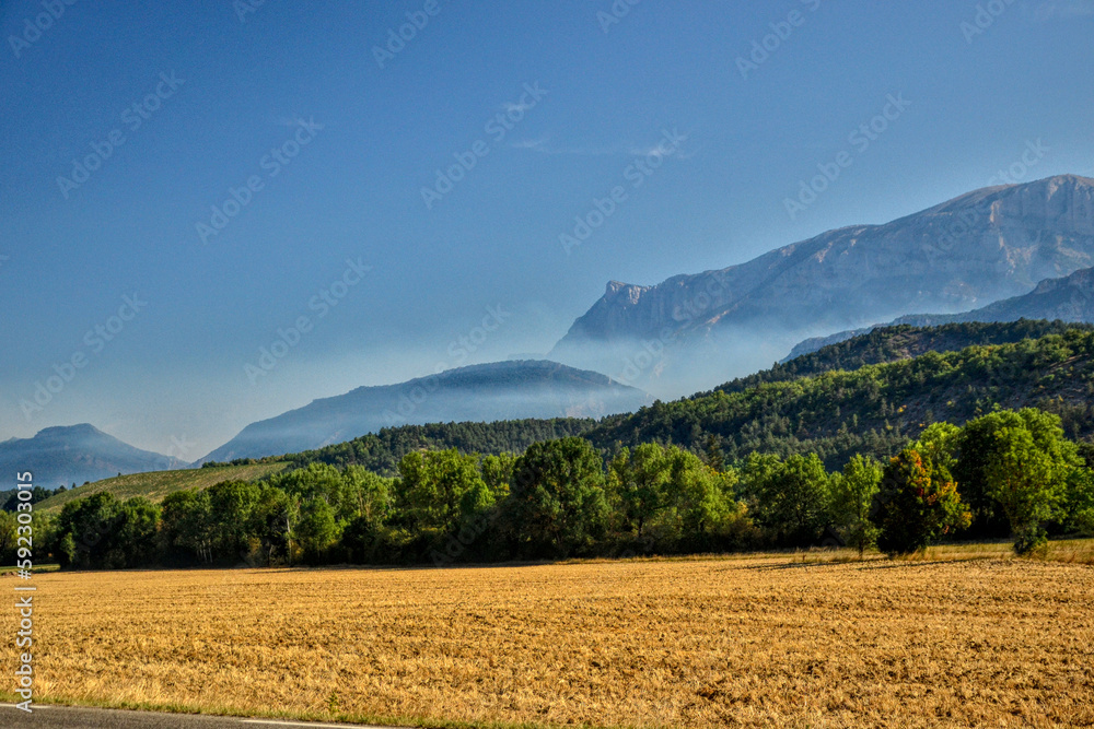 Die, France - August 10th 2022 : Landscape representing a field of mowed wheat. In background, there is a mountain range. White smoke is that of a forest fire, caused by a flash during a thunderstorm