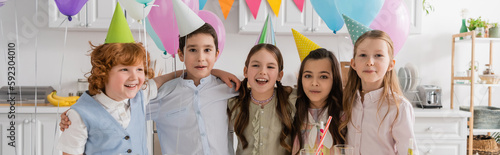 Photography positive group of children singing happy birthday song next to cake with candles and balloons, banner