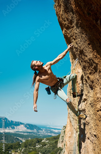 Power and energy in human body. Athletic confidence man climber looking up and gripping hold. Rock climbing and active lifestyle concept