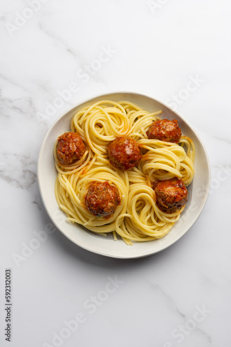 Pasta with meat balls on a plate on a marble white background. Cooking spaghetti with tomato sauce, vegetables, cheese and meatballs. Step by step. Step 2 Pasta with meatballs.