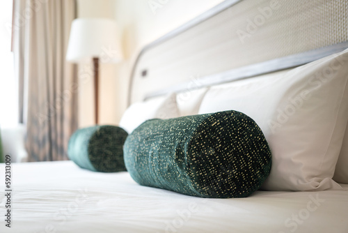 A green bolster cushion pillow is placed on the bed in luxury bed room. Interior decoration object photo, selective focus. photo