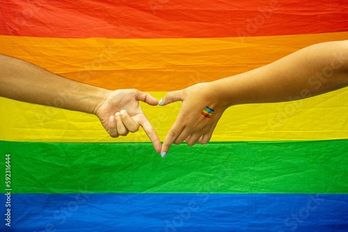 Human hands make heart shape in background of LGBT flag
