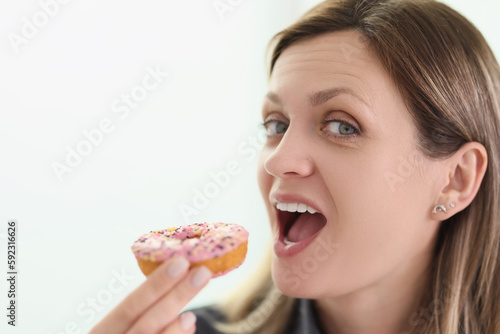 Woman bites delicious donut with glaze looking in camera