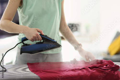 Housewife irons red blouse with hot steam appliance at home