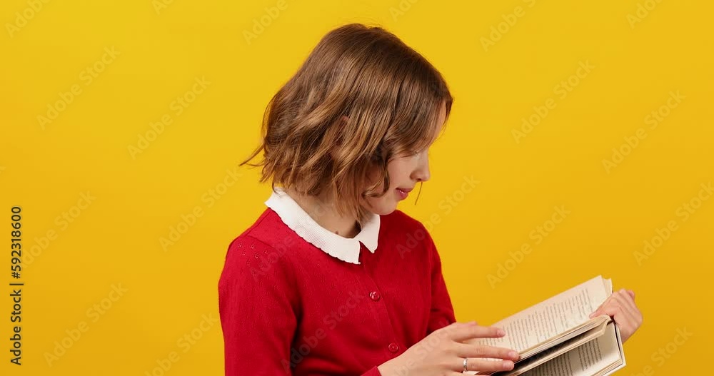 Happy schoolgirl reading a book on yellow studio background Happy schoolgirl reading a book on yellow studio background