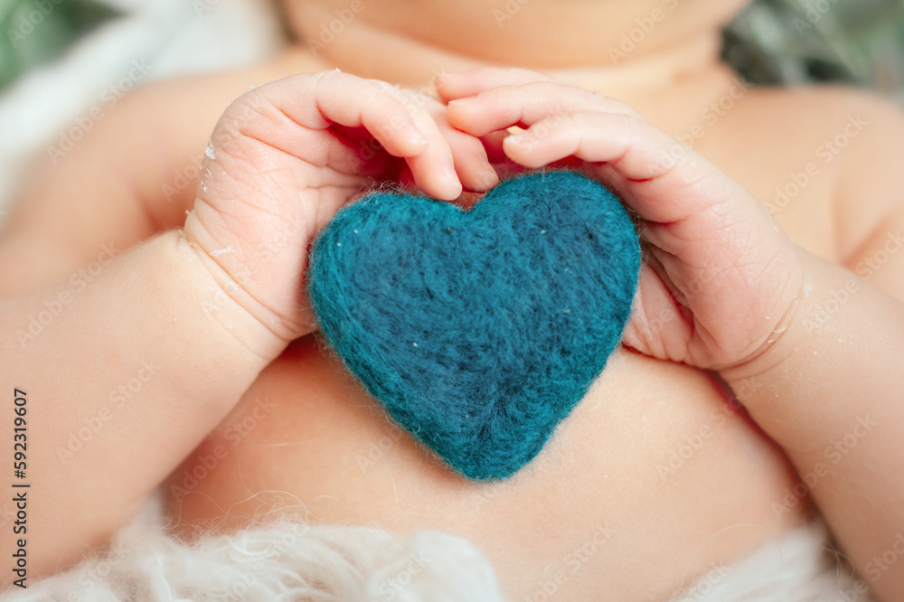 The hand and fingers of a newborn. The hand and fingers of a newborn. Baby holding a knitted heart with his fingers The hand and fingers of a newborn. The hand and fingers of a newborn. Baby holding a knitted heart with his fingers