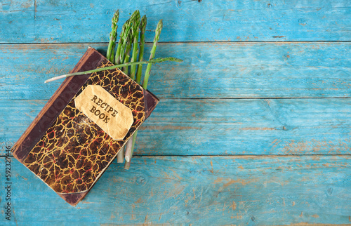 bunch of fresh green asparagus and old recipe book on wooden background, seasonal food cooking and healthy eating concept photo