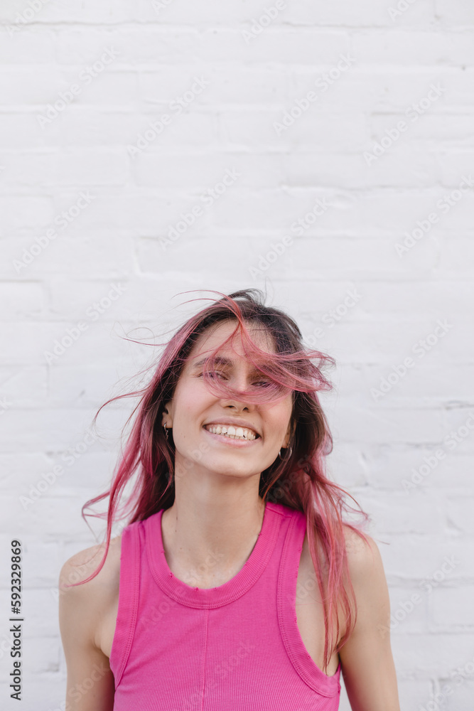 Positive pink hair woman in pink top. Portrait of happy attractive lady at background of white brick wall. Teeth smile woman look at camera, flying hair on the wind, hair on face. Positive pink hair woman in pink top. Portrait of happy attractive lady at background of white brick wall. Teeth smile woman look at camera, flying hair on the wind, hair on face.