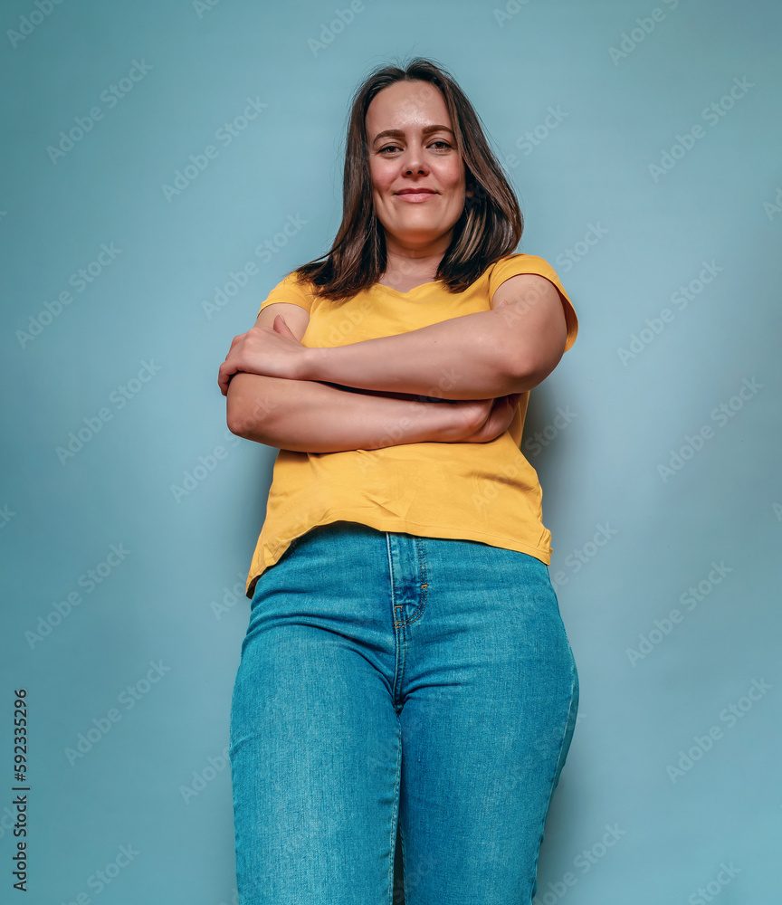 Lower angle young woman crossed arms on blue studio background Lower angle young woman crossed arms on blue studio background