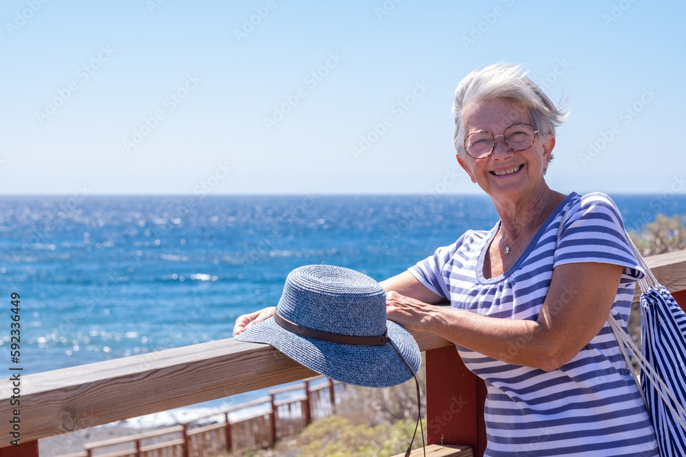 Fototapeta premium Happy cheerful senior woman in outdoors summer sea. White haired smiling lady dressed in blue expressing freedom and joy. Horizon over water