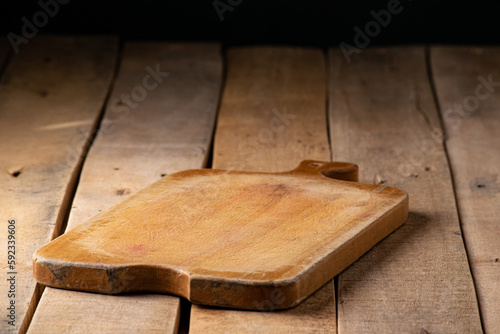 Rustic wooden chopping board on rustic wooden table in black background