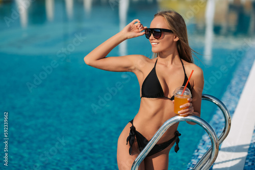 Tanned legs near the swimming pool. Beautiful girl going to swim. A young woman stands by a ladder in a swimming pool during the golden hour. Relaxing on summer holiday near water