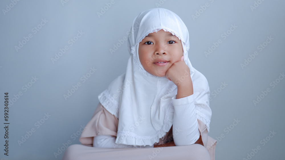 moslem young girl sitting and thinking pose over gray background moslem young girl sitting and thinking pose over gray background