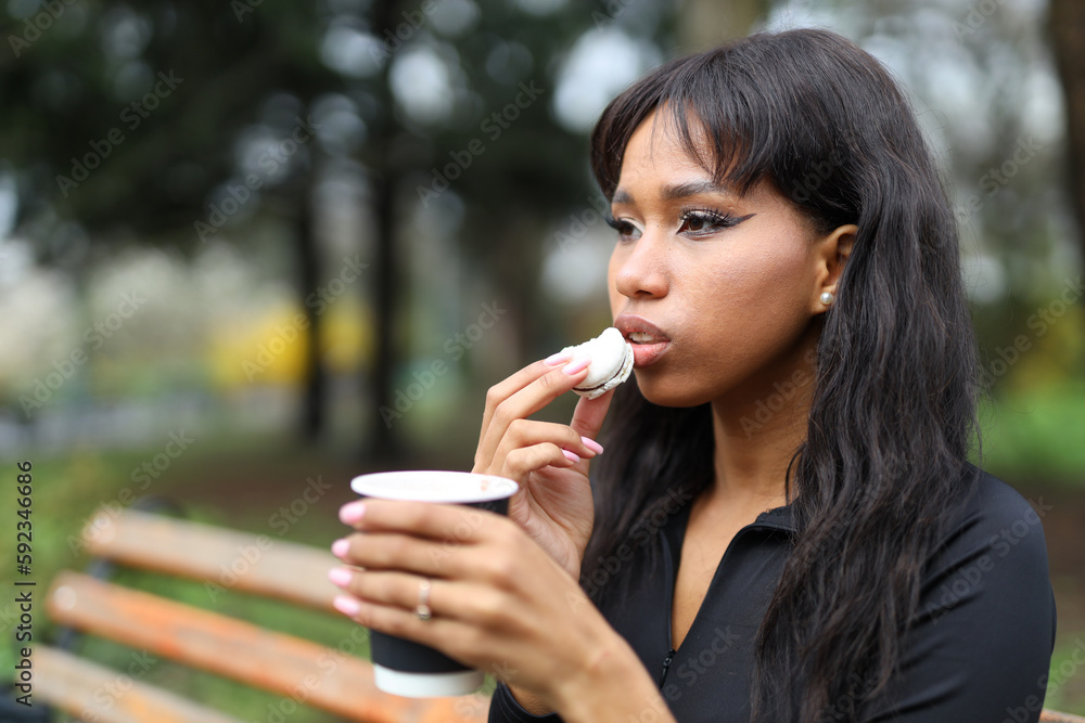 Portrait of an African woman who eats macaroons with coffee in the park. Portrait of an African woman who eats macaroons with coffee in the park.