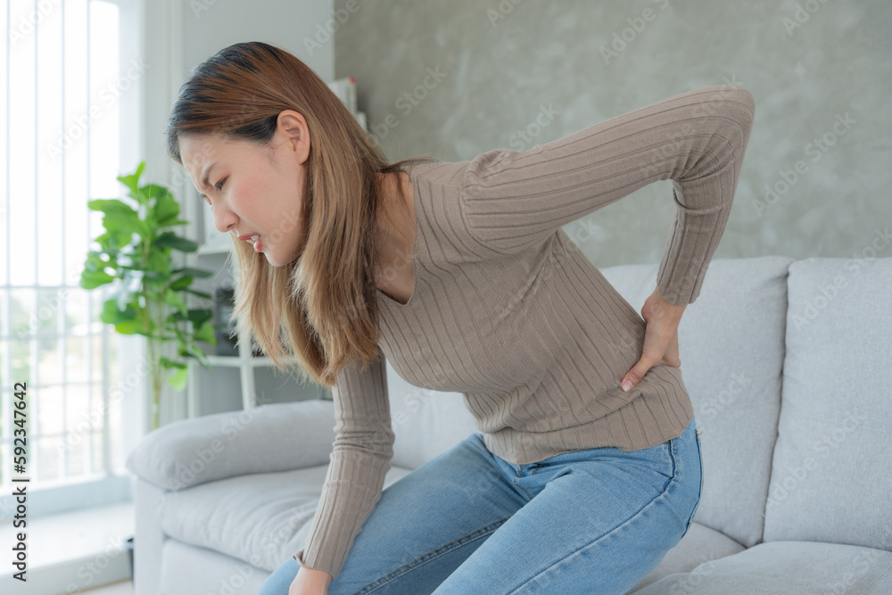 Asia beautiful woman holding her lower back while and suffering from unbearable pain health and problems, chronic back pain, backache in office syndrome, scoliosis, herniated disc, muscle inflammation Asia beautiful woman holding her lower back while and suffering from unbearable pain health and problems, chronic back pain, backache in office syndrome, scoliosis, herniated disc, muscle inflammation