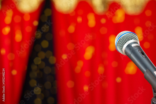 Um microfone preto, em um palco com cortina vermelha desfocada ao fundo. photo