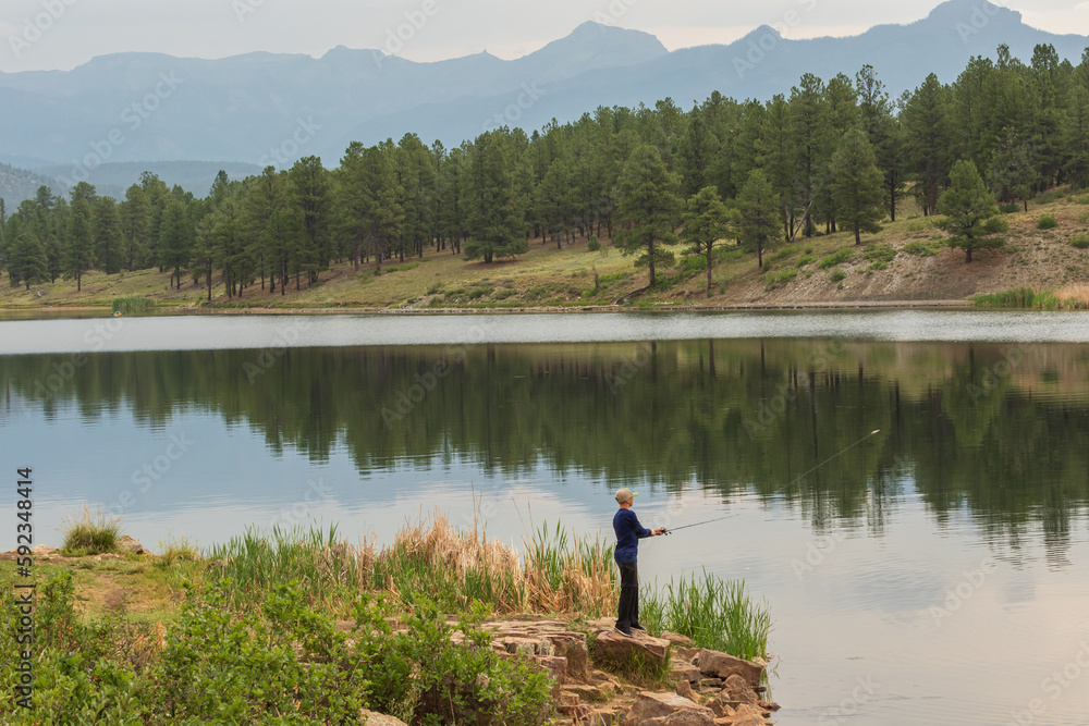 Obraz premium A young male is fishing on a beautiful mountain lake in Colorado in the United States.