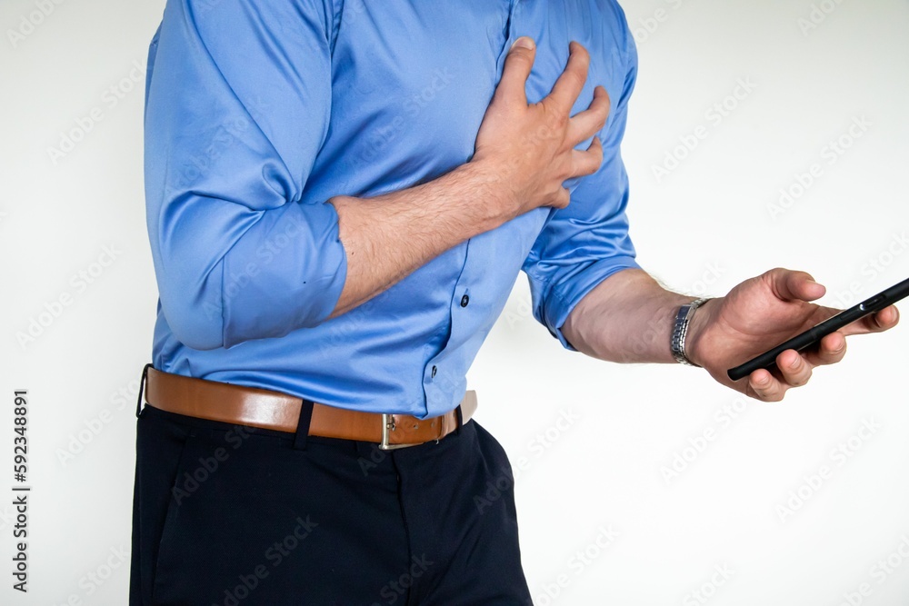 Man holding a phone in one hand while his other hand is on his chest indicating receiving bad news Man holding a phone in one hand while his other hand is on his chest indicating receiving bad news