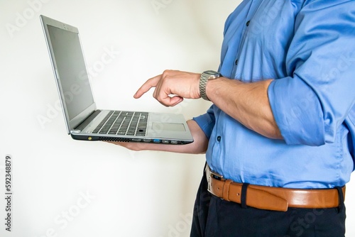 Closeup shot of a man holding a laptop and pointing at the screen while wearing a blue formal shirt