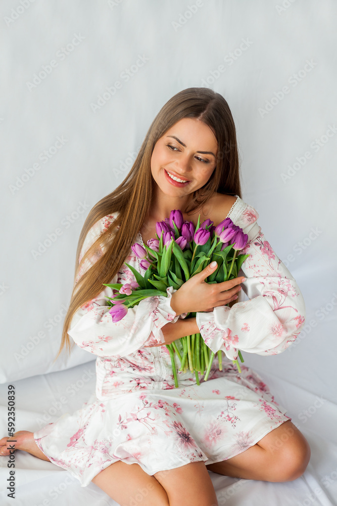 Portrait of sexy beautiful young woman with long hair. Model with a bouquet of lilac tulips on white. Spring. Holidays.