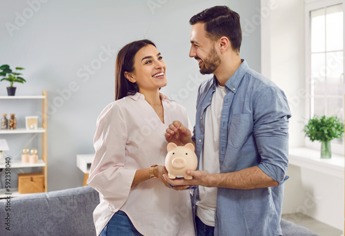 Smiling, happy young family together put coins in piggy bank to save money. Married couple are planning to save up finances. Savings, investments, financial freedom, business, hope for success. photo