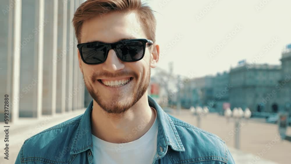 Portrait of handsome smiling stylish hipster lumbersexual model. Man dressed in jeans jacket clothes. Fashion male posing on the street background in sunglasses Portrait of handsome smiling stylish hipster lumbersexual model. Man dressed in jeans jacket clothes. Fashion male posing on the street background in sunglasses