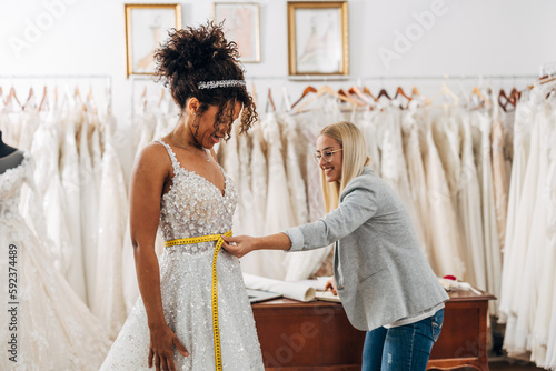 Cuadro en lienzo A caucasian tailor is measuring waist size on a beautiful multiracial bride in a
