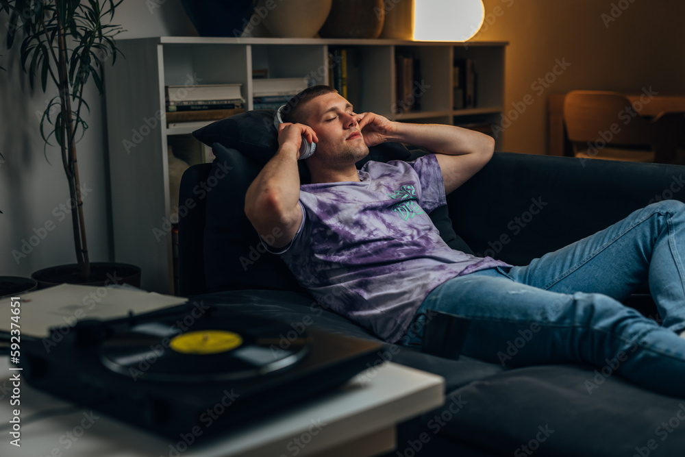 Fototapeta premium A Caucasian man puts on headphones to listen to records and relax at night