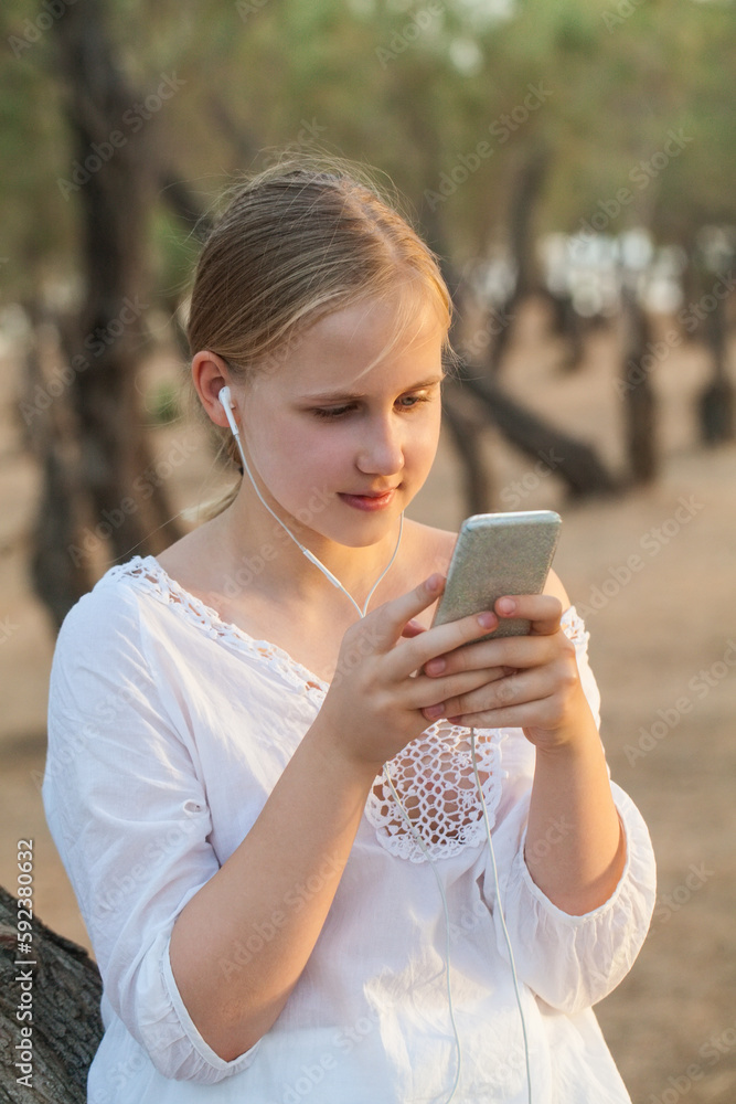 Teenage girl in headphones holding mobile phone on the background of forest Teenage girl in headphones holding mobile phone on the background of forest