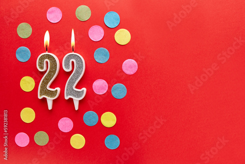 Number 22 on a red background with colored confetti. Happy birthday candles. The concept of celebrating a birthday, anniversary, important date, holiday. Copy space. banner