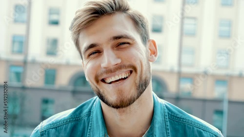 Portrait of handsome smiling stylish hipster lumbersexual model. Man dressed in jeans jacket clothes. Fashion male posing on the street background photo