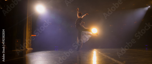 Full shot of ballet dancers practicing ballet movements and rehearse choreography on classic theater stage illuminated by spotlights. Dance partners prepare theatrical performance. Classical ballet. © Framestock