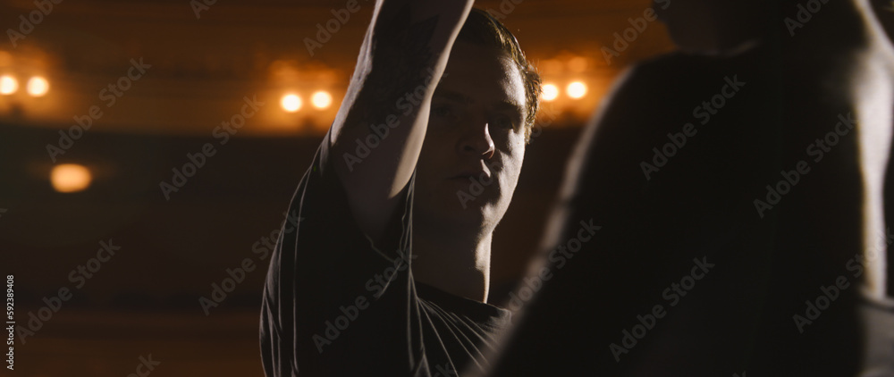 Close up shot of ballet dancers practicing and rehearsing choreography on classic theater stage illuminated by spotlights. Partners prepare for theatrical dance performance. Classical ballet dance.