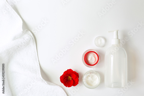 A set of creams, a red flower and a white towel are on a white background. Spa and cometology theme. Copy space.
