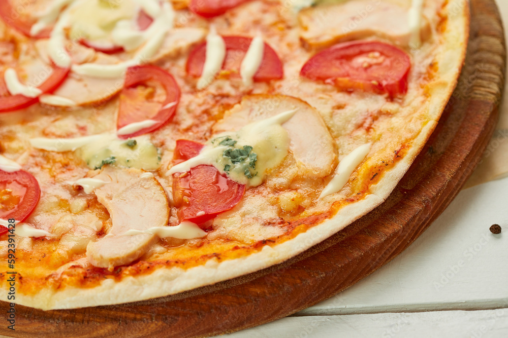 Freshly baked pizza with smoked chicken fillet and gorgonzola cheese served on wooden background with tomatoes, sauce and herbs. Food delivery concept. Restaurant menu