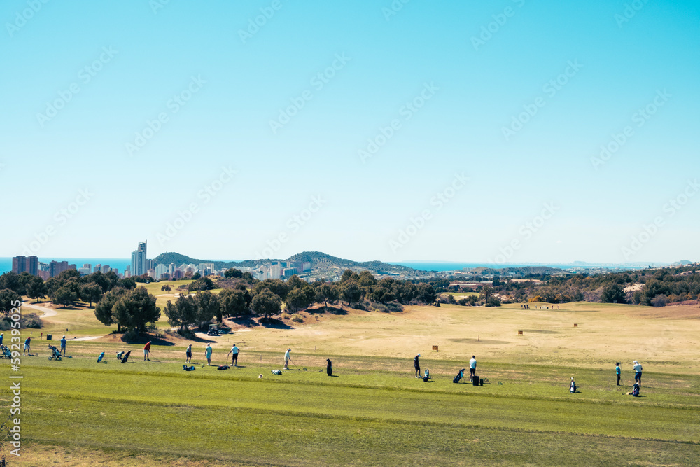 Active leisure in Benidorm, Spain. People are playing golf in golf course on sunny day with the skyscrapers of Benidorm and the Mediterranean Sea in the background