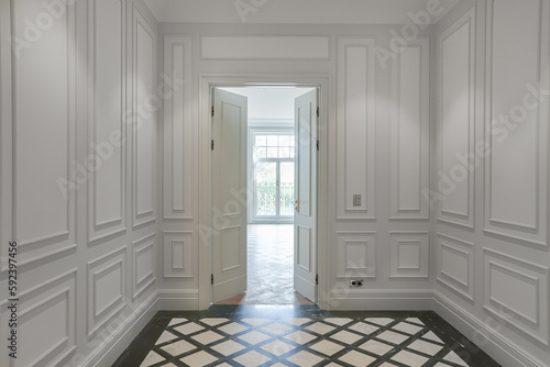 interior in an apartment with a classic luxury design, white walls with a panel, a view of the corridor, an open door and an empty room with a large window