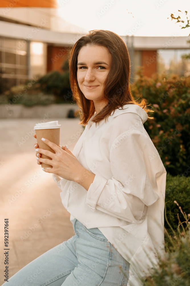Young calm woman is having a break outdoors with a take away cup of coffee. Vertical shot. Young calm woman is having a break outdoors with a take away cup of coffee. Vertical shot.