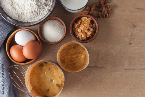 Preparation for cooking sweet pastries. Dough, eggs, sugar, milk, flour, salt, candied fruits, raisins, nuts, whisk on the kitchen table. copy space