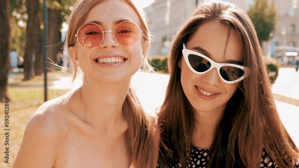 Portrait of two young beautiful smiling hipster girls in trendy summer clothes.Carefree women posing on street background. Positive models having fun in sunglasses and blowing bubble with chewing gum Portrait of two young beautiful smiling hipster girls in trendy summer clothes.Carefree women posing on street background. Positive models having fun in sunglasses and blowing bubble with chewing gum