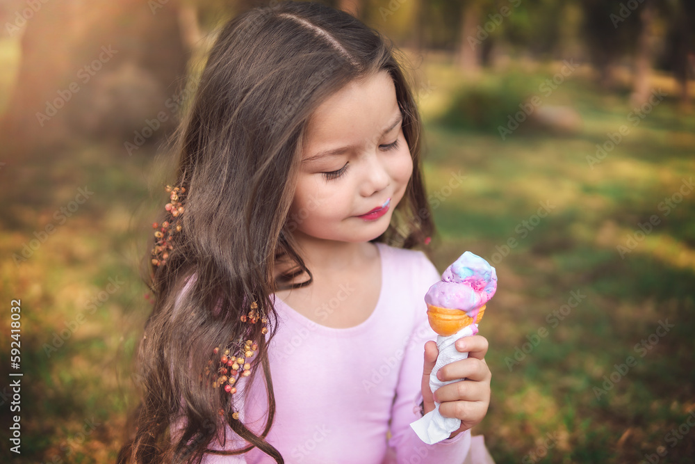 Cute blonde curly-haired girl eating a nice ice cream in the park, concept of children's day