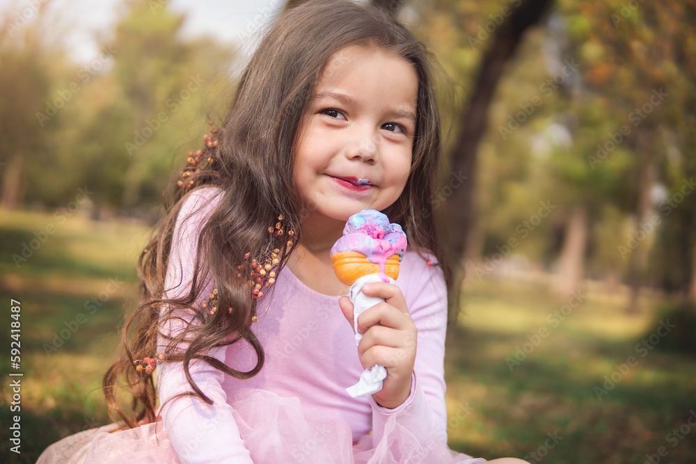Cute blonde curly-haired girl eating a nice ice cream in the park, concept of children's day Cute blonde curly-haired girl eating a nice ice cream in the park, concept of children's day