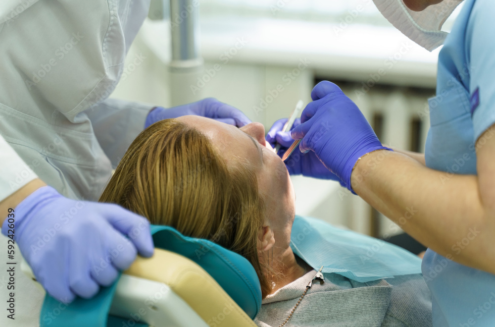 A doctor examines a woman's teeth with a dental instrument. A doctor examines a woman's teeth with a dental instrument.