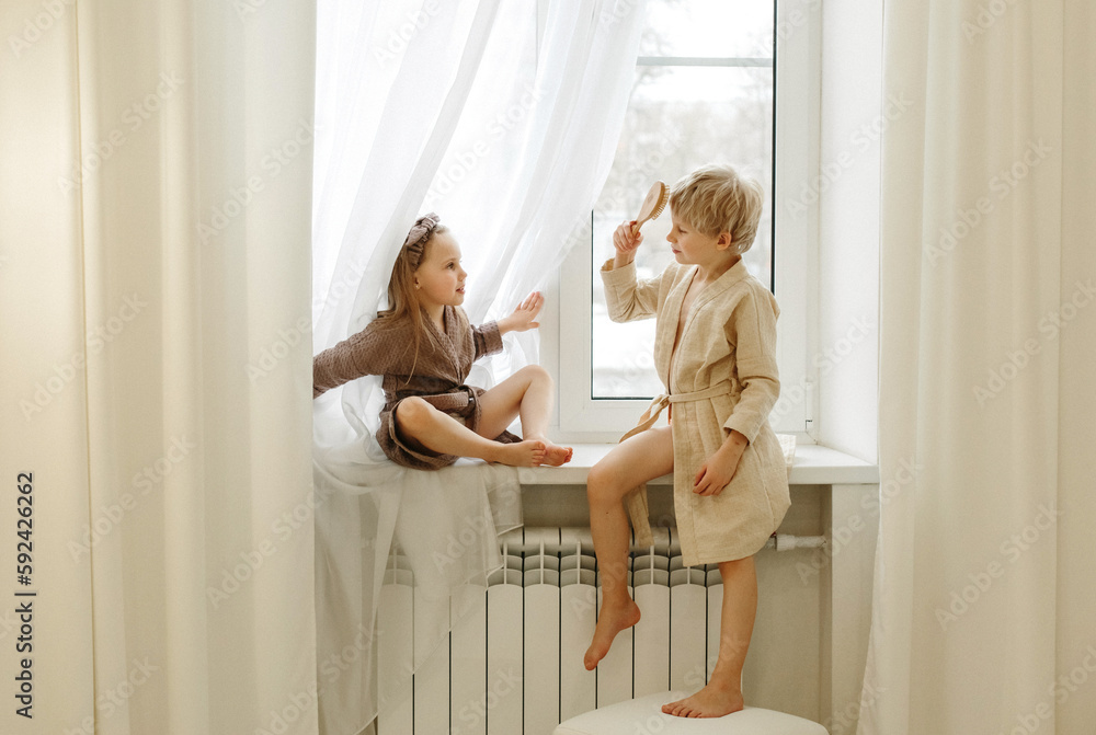 Obraz premium A boy and a girl are sitting on the windowsill in the bedroom, talking and playing