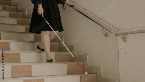 Woman with blindness disability walking down stairs using blind walking stick or long cane and touching stair handrail